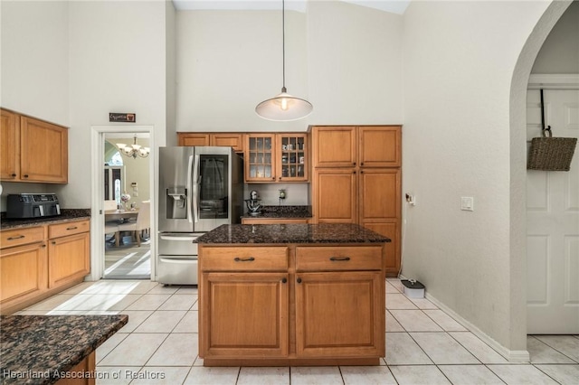 kitchen with dark stone counters, a high ceiling, stainless steel refrigerator with ice dispenser, decorative light fixtures, and light tile patterned flooring