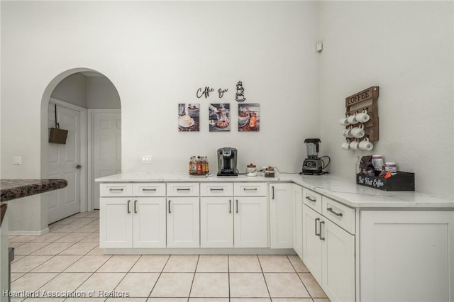 kitchen with kitchen peninsula, white cabinetry, light tile patterned flooring, and light stone countertops