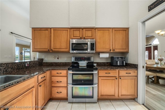 kitchen with light tile patterned floors, sink, stainless steel appliances, and dark stone countertops