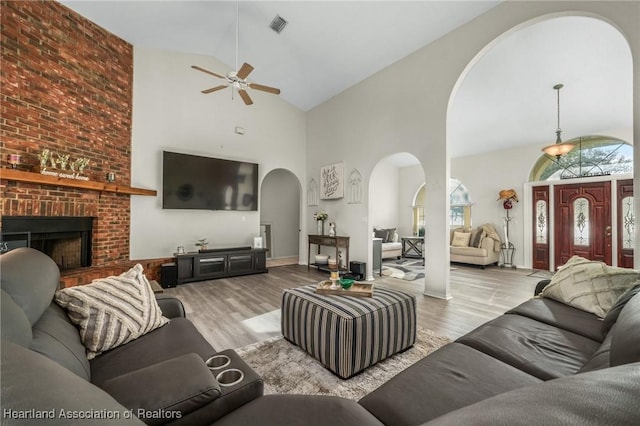 living room with ceiling fan, light hardwood / wood-style flooring, high vaulted ceiling, and a brick fireplace