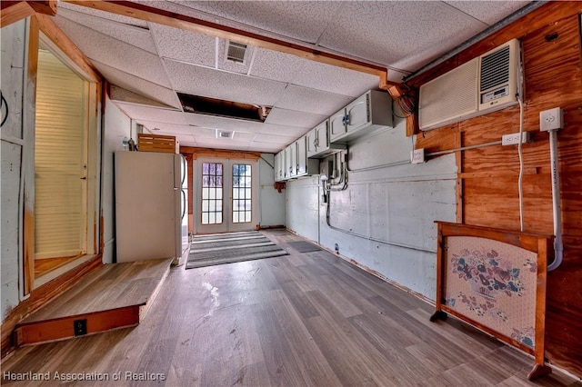 basement with wood finished floors, visible vents, freestanding refrigerator, a wall mounted AC, and a paneled ceiling