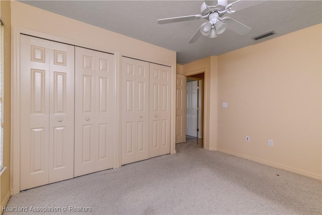 unfurnished bedroom featuring ceiling fan, two closets, and a textured ceiling