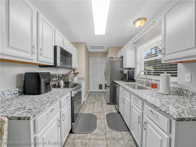 kitchen with light stone counters, visible vents, a sink, stainless steel appliances, and white cabinetry