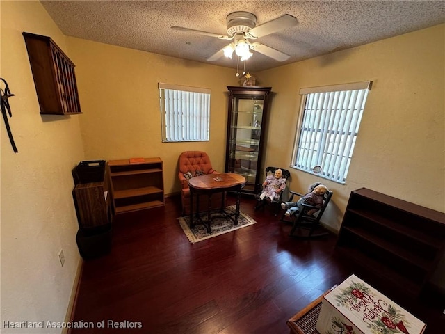 living area featuring ceiling fan, dark hardwood / wood-style floors, and a textured ceiling