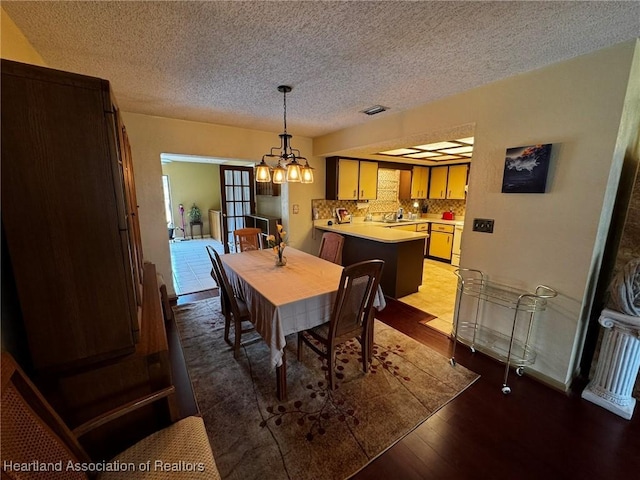 dining area with sink, a textured ceiling, a notable chandelier, and light hardwood / wood-style floors