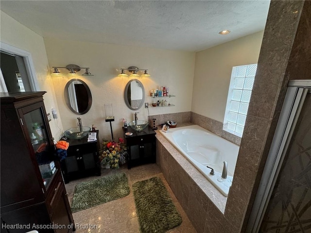 bathroom featuring vanity, a textured ceiling, and tiled tub