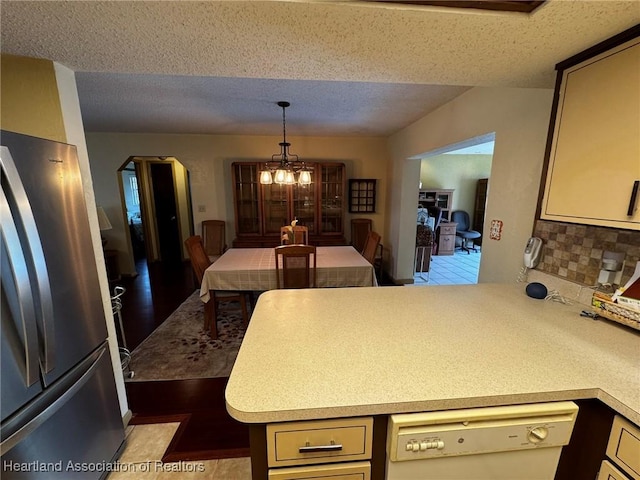 kitchen featuring cream cabinetry, stainless steel fridge, kitchen peninsula, and white dishwasher