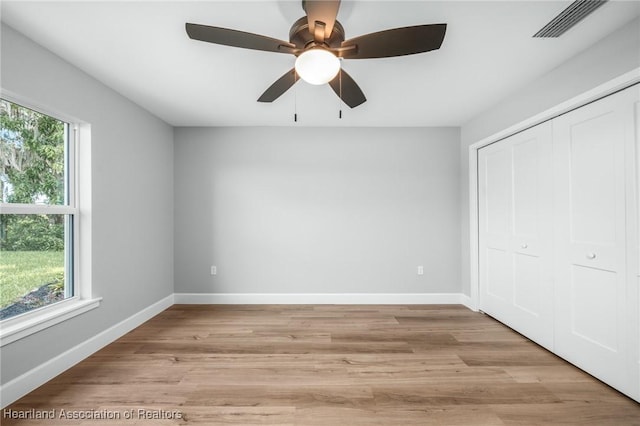 unfurnished bedroom featuring multiple windows, ceiling fan, a closet, and light wood-type flooring