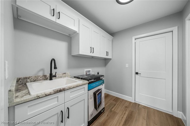 kitchen with light stone countertops, light hardwood / wood-style flooring, white cabinetry, and sink