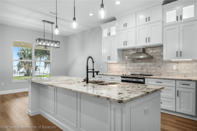 kitchen featuring white cabinets, sink, wall chimney exhaust hood, and an island with sink