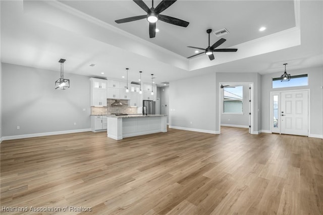 unfurnished living room with ceiling fan, a raised ceiling, and light wood-type flooring