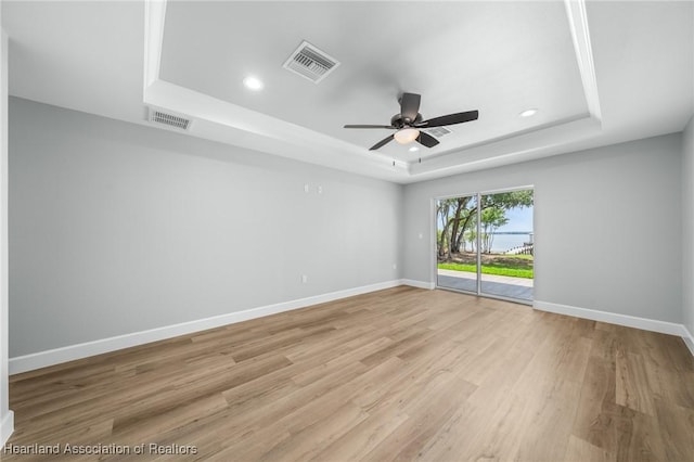 empty room with ceiling fan, light hardwood / wood-style flooring, and a tray ceiling