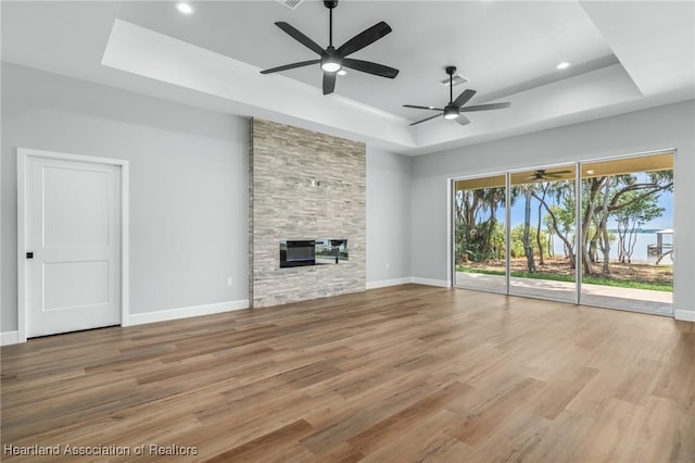 unfurnished living room with a tray ceiling, ceiling fan, a fireplace, and light hardwood / wood-style floors