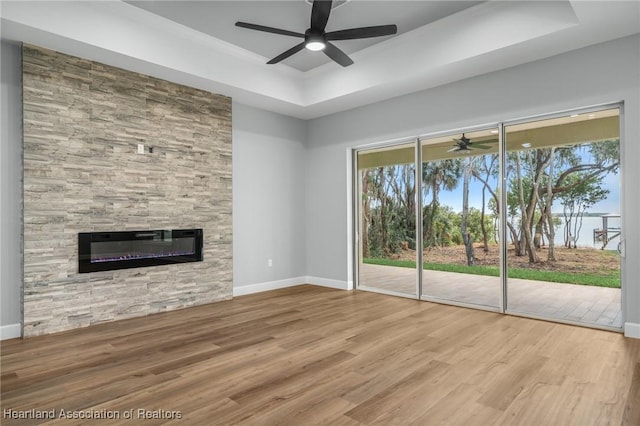 unfurnished living room featuring a raised ceiling, a tile fireplace, ceiling fan, and hardwood / wood-style flooring