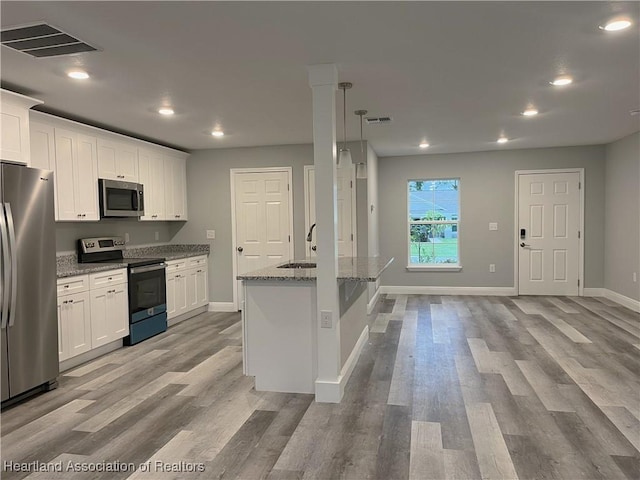 kitchen with light stone countertops, stainless steel appliances, white cabinetry, and a kitchen island with sink