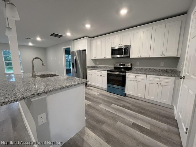 kitchen with light wood-type flooring, light stone counters, stainless steel appliances, sink, and white cabinets