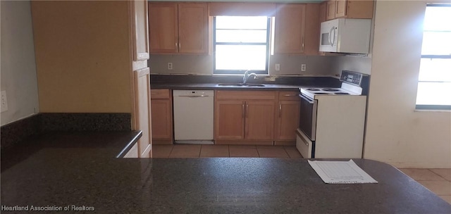 kitchen with dark countertops, white appliances, a sink, and light tile patterned flooring