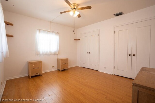 unfurnished bedroom featuring a ceiling fan, visible vents, baseboards, light wood-style floors, and multiple closets