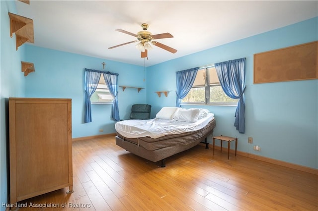 bedroom featuring multiple windows, wood finished floors, baseboards, and ceiling fan