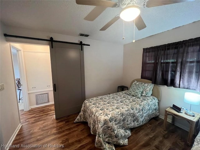 bedroom featuring a barn door, ceiling fan, wood-type flooring, and a textured ceiling