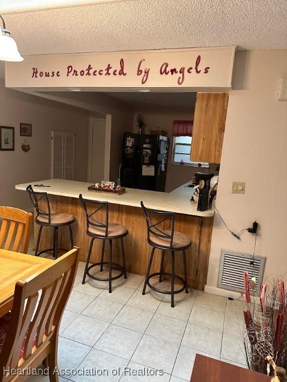 bar with light tile patterned flooring, black fridge, and a textured ceiling