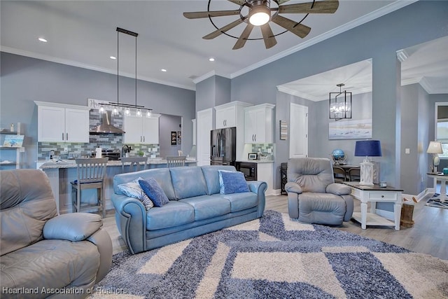 living area with ornamental molding, recessed lighting, light wood-style flooring, and ceiling fan with notable chandelier