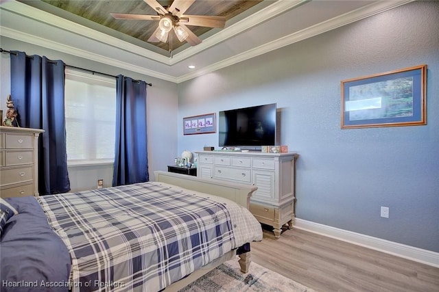 bedroom featuring light wood finished floors, ceiling fan, a tray ceiling, baseboards, and ornamental molding