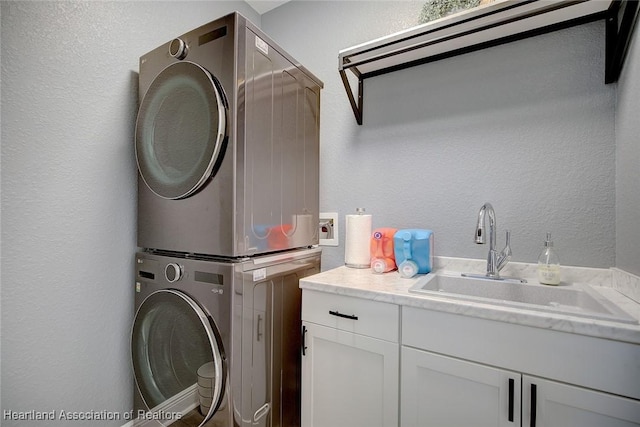 laundry area featuring stacked washer and dryer, a sink, a textured wall, and cabinet space