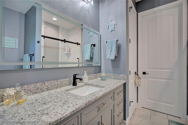full bathroom featuring a stall shower, marble finish floor, a textured wall, and vanity