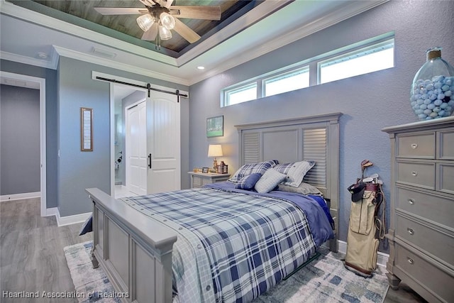 bedroom featuring light wood finished floors, a barn door, a raised ceiling, visible vents, and baseboards
