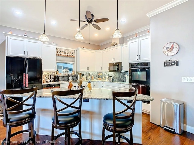 kitchen featuring tasteful backsplash, light stone counters, black appliances, a center island, and white cabinetry