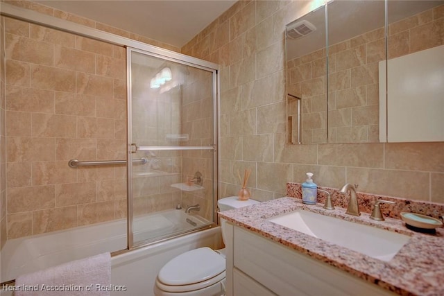 bathroom with toilet, vanity, decorative backsplash, enclosed tub / shower combo, and tile walls