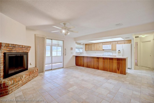 kitchen featuring white appliances, a ceiling fan, a peninsula, a fireplace, and light countertops