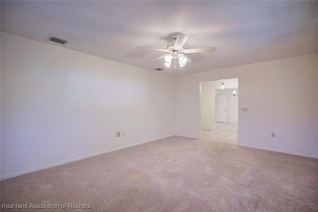 empty room featuring a textured ceiling, light colored carpet, visible vents, and ceiling fan