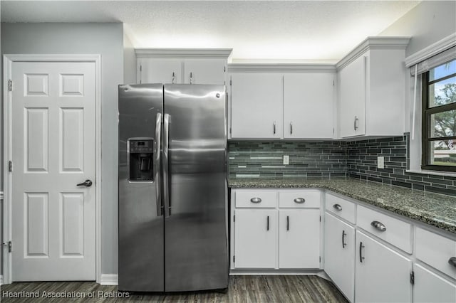 kitchen with white cabinets, stainless steel fridge, backsplash, and dark stone counters