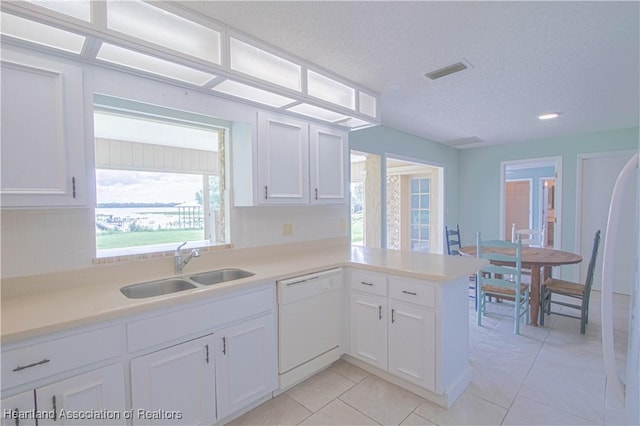 kitchen with kitchen peninsula, white cabinets, sink, light tile patterned floors, and dishwasher