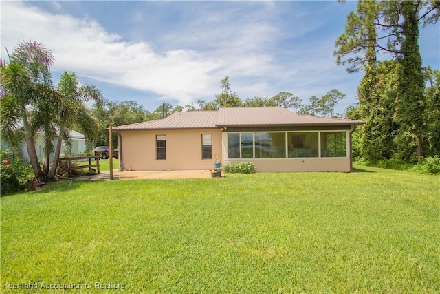 rear view of property featuring a lawn, a sunroom, and a patio area