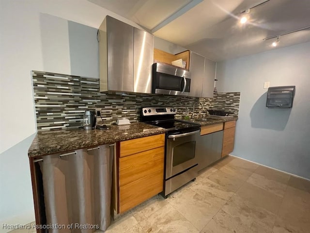 kitchen featuring sink, tasteful backsplash, dark stone counters, track lighting, and appliances with stainless steel finishes