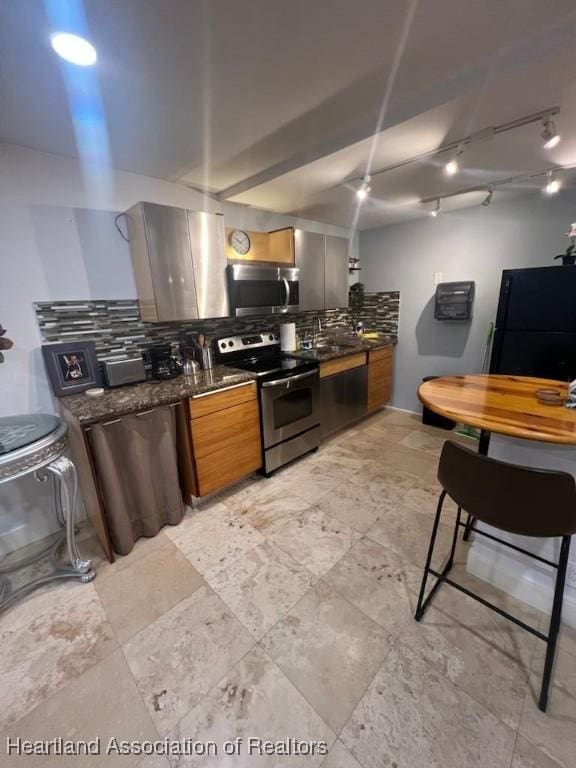 kitchen with brown cabinets, stainless steel appliances, tasteful backsplash, a sink, and dark stone counters