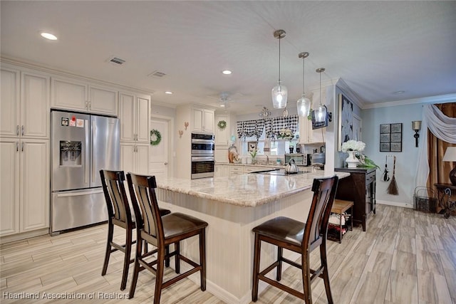 kitchen featuring a breakfast bar, light stone countertops, appliances with stainless steel finishes, decorative light fixtures, and white cabinetry