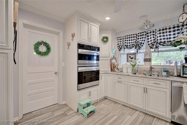 kitchen with appliances with stainless steel finishes, light stone counters, ornamental molding, sink, and white cabinets