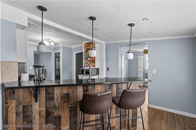 kitchen featuring kitchen peninsula, ornamental molding, sink, white cabinetry, and hanging light fixtures