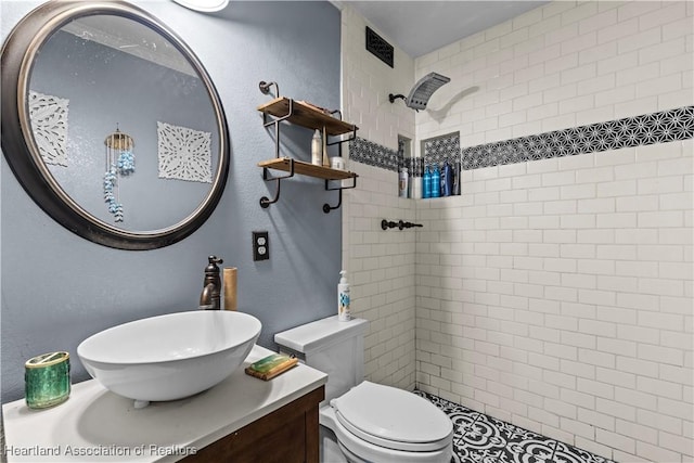 bathroom with tiled shower, vanity, and toilet