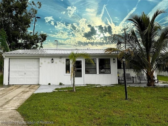 view of front of property featuring a garage, metal roof, concrete driveway, and a front yard