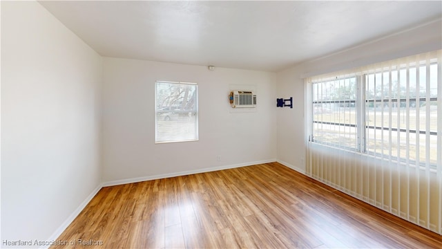 unfurnished room featuring baseboards, an AC wall unit, and wood finished floors