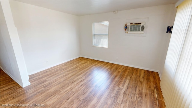 spare room featuring light wood-type flooring, baseboards, and an AC wall unit