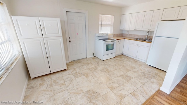 kitchen with white cabinetry, white appliances, baseboards, and a sink