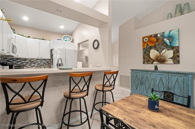 kitchen with white appliances, light tile patterned floors, a peninsula, white cabinetry, and visible vents
