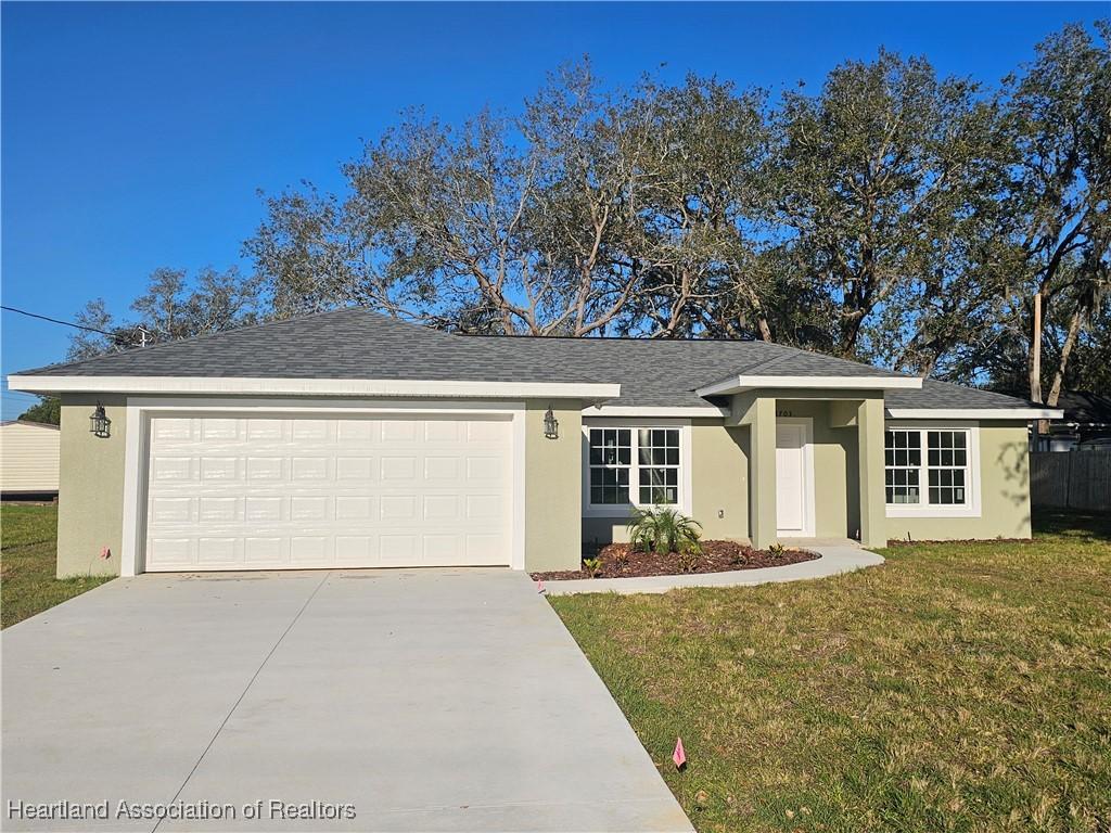 ranch-style house with roof with shingles, an attached garage, stucco siding, concrete driveway, and a front lawn