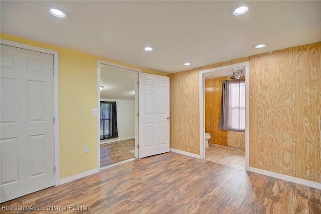 unfurnished bedroom featuring connected bathroom, wood walls, and hardwood / wood-style floors